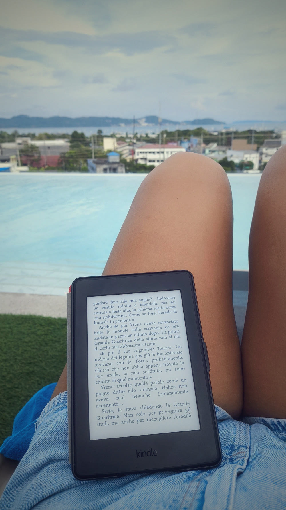 Un e-reader appoggiato sulle gambe a bordo piscina